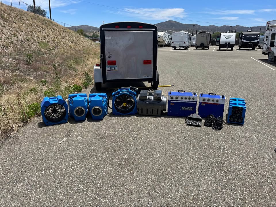 Used electric heaters, air movers, and equipment laid out in front of an enclosed trailer.